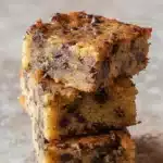 Chocolate Chip Banana Bars 9 Stack of three chocolate chip banana bars with golden tops and gooey chocolate chips on dark slate surface