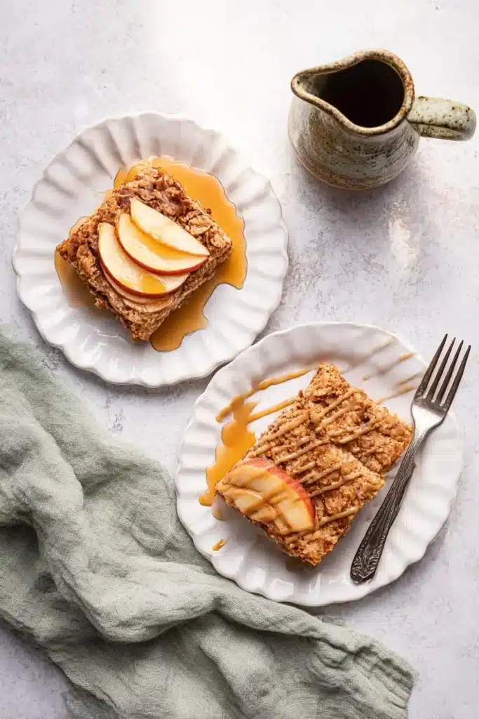 Oatmeal Apple Breakfast Bake – Cozy & Vegan Delight 6 Two slices of oatmeal apple breakfast bake with almond butter drizzle and apple toppings on white plates