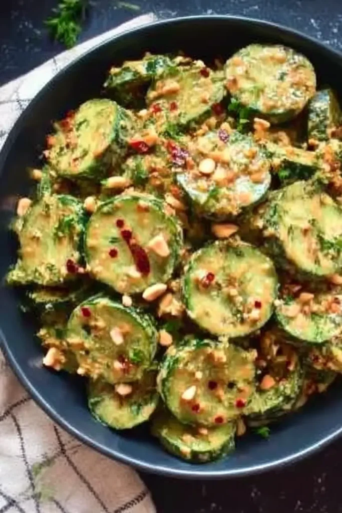 Top-down view of cucumbers in spicy peanut sauce topped with peanuts, chili flakes, and parsley