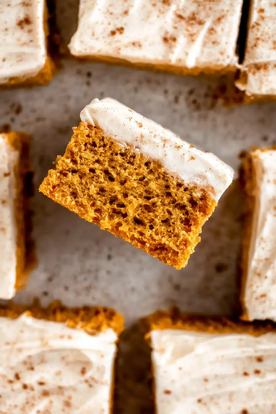 Moist pumpkin bars with cream cheese frosting and cinnamon, one lifted to show soft texture.