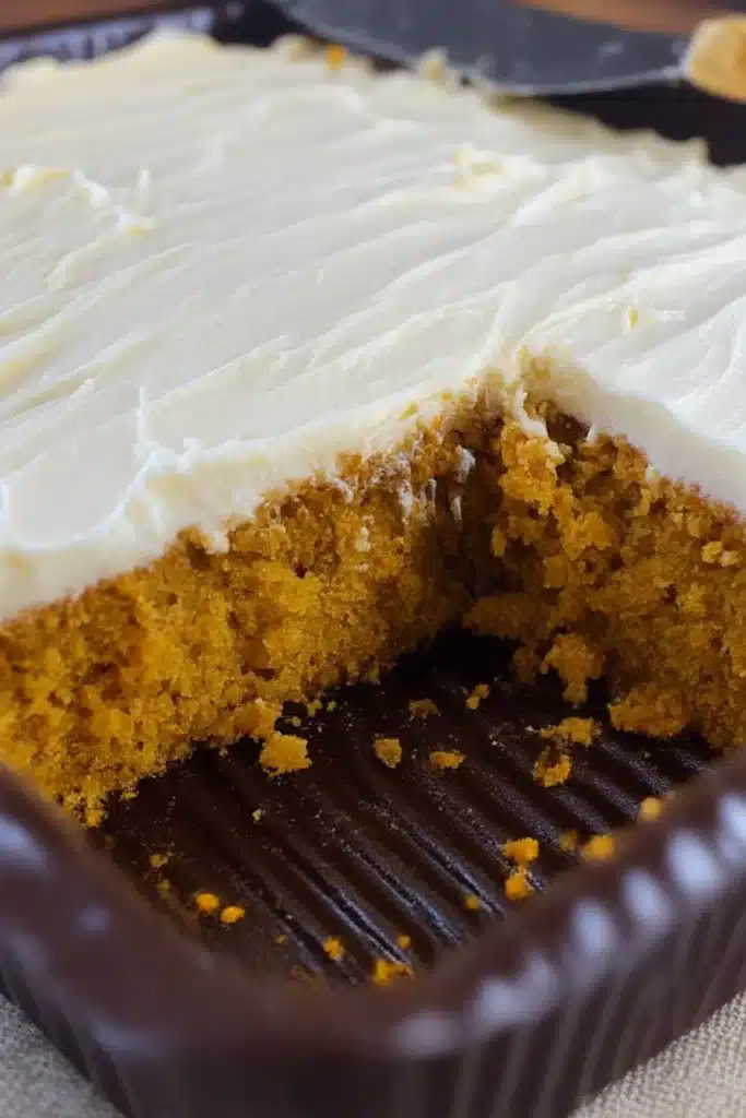 Easy Pumpkin Carrot Cake Recipe That’s Cozy and Quick 8 Partially sliced pumpkin carrot cake in baking pan with cream cheese frosting