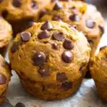 Pumpkin Chocolate Chip Muffins 8 Close-up of moist pumpkin chocolate chip muffin topped with melted chocolate chips on parchment paper.