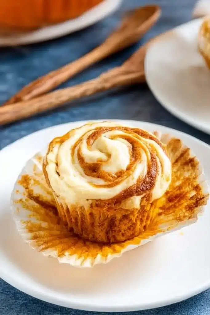 Pumpkin cream cheese muffin with creamy swirl and crumb-stained liner on a white plate

