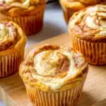 Pumpkin cream cheese muffins with creamy swirl tops on a wooden board over a white table