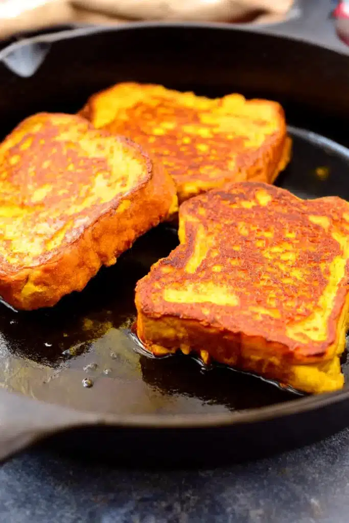 Pumpkin French toast slices cooking in a black skillet on a rustic stone surface

