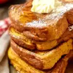 Stack of pumpkin French toast with melted butter, powdered sugar, and maple syrup on a plate