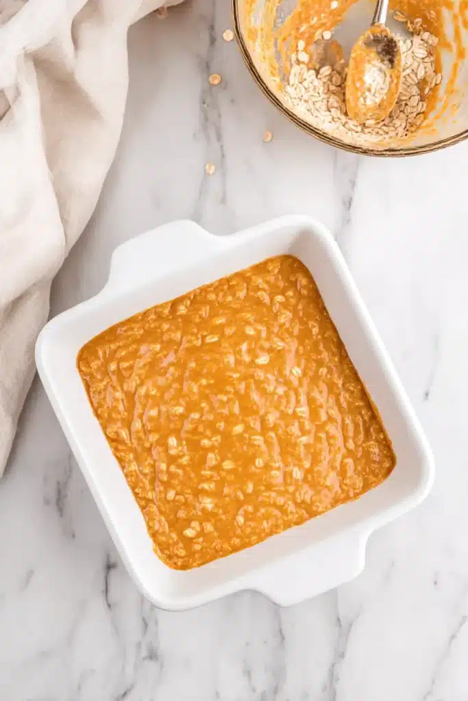 Pumpkin Baked Oatmeal 12 White ceramic baking dish filled with pumpkin oatmeal batter ready for oven, on rustic stone surface