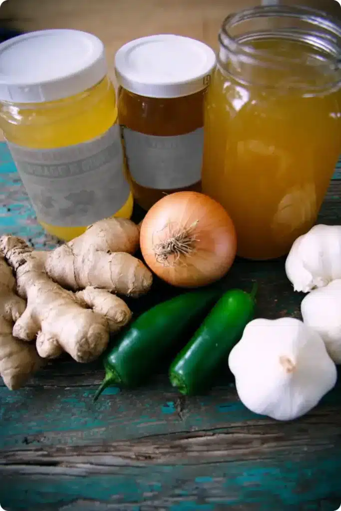 Raw fire cider ingredients on rustic table including ginger, garlic, onion, apple cider vinegar, and jalapeño