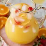 Breakfast Punch | Refreshing & Crowd-Pleasing Brunch Drink 7 Glass pitcher of breakfast punch with citrus slices, ice cubes, and strawberries on a pastel surface