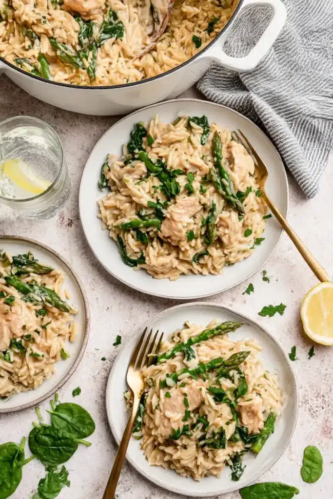 Creamy chicken orzo plated with asparagus, parmesan, and parsley, served with lemon water and rustic table styling