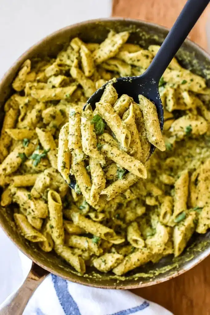 Creamy Chicken Pesto Pasta | Amazing Weeknight Dinner 7 Serving spoon lifting creamy chicken pesto pasta from skillet with tender chicken and pesto sauce