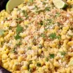 Skillet Mexican Street Corn — A Quick, Flavorful Summer Side 6 Close-up of creamy skillet Mexican street corn with cotija cheese, cilantro, and lime wedges in a rustic cast iron pan