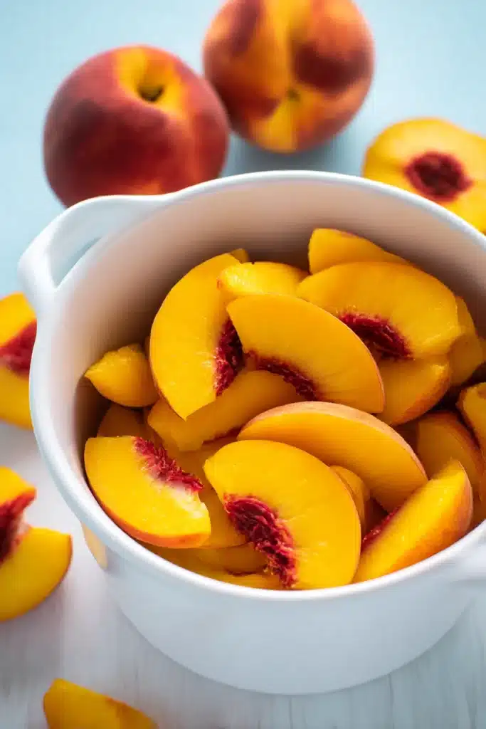 Amazing Fresh Peach Margaritas Recipe | Quick & Refreshing 10 Fresh peach slices in a white bowl with whole peaches on pale wooden table