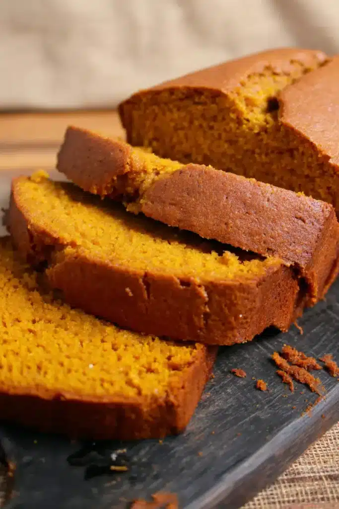 Sliced Pumpkin Bread recipe loaf showing golden crust and soft moist orange interior on rustic slate surface.