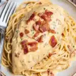 Slow Cooker Crack Chicken served over creamy cheddar ranch spaghetti with bacon bits on a rustic plate