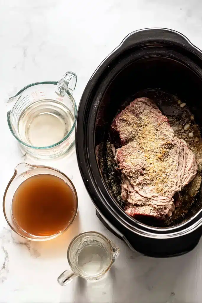 Raw beef roast in a slow cooker with onion soup mix and broth ingredients