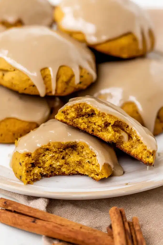 Moist pumpkin cookie broken in half with maple glaze and warm fall spices in the background.