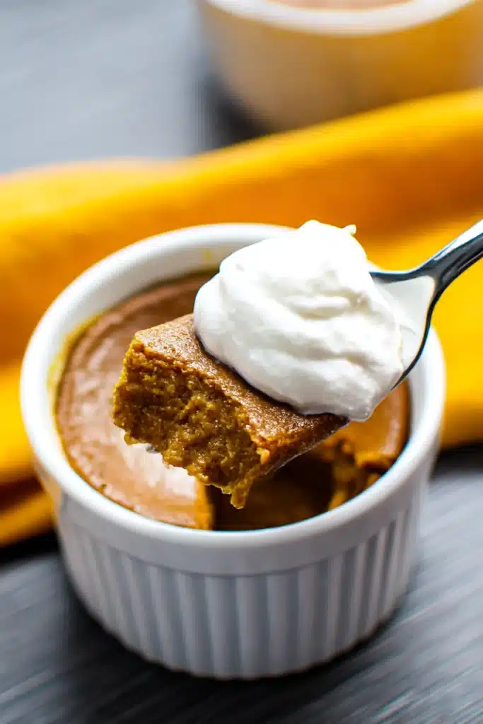 Spoonful of Mini Keto Crustless Pumpkin Pie with whipped cream from white ramekin