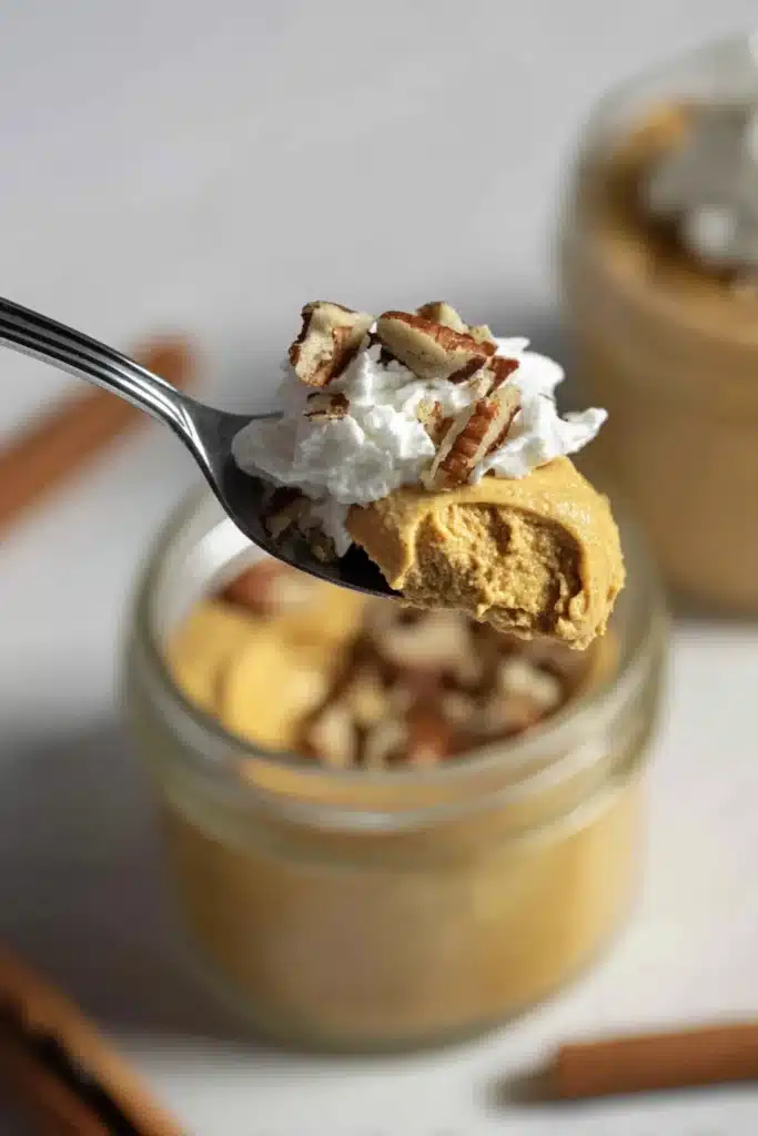 Pumpkin Fluff – Light, Easy & Delicious 11 Close-up of pumpkin fluff on a spoon with pecans and whipped cream above a jar