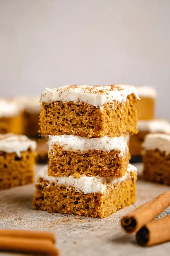 Stack of moist pumpkin bars with cream cheese frosting and cinnamon sticks.