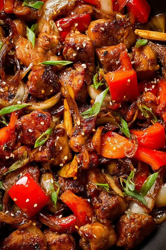 Close-up of chili crisp chicken stir-fry with glazed chicken, red peppers, onions, and sesame seeds in spicy sauce.