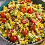 Colorful summer corn salad with avocado, cherry tomatoes, red onion, cilantro, served in a rustic bowl.