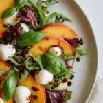 Fresh summer peach salad with basil, mozzarella, and mixed greens on a ceramic plate