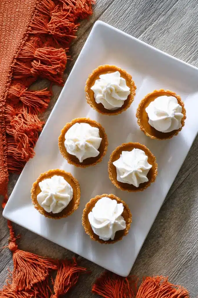 Overhead shot of mini keto pumpkin pies with whipped cream, served on a white platter with a cozy fall napkin.