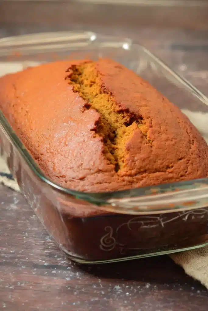 Whole pumpkin bread loaf in glass baking dish with golden crust on rustic slate surface.