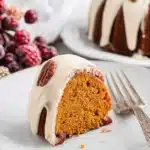 Slice of keto pumpkin bundt cake with cream cheese icing and pecan on a plate