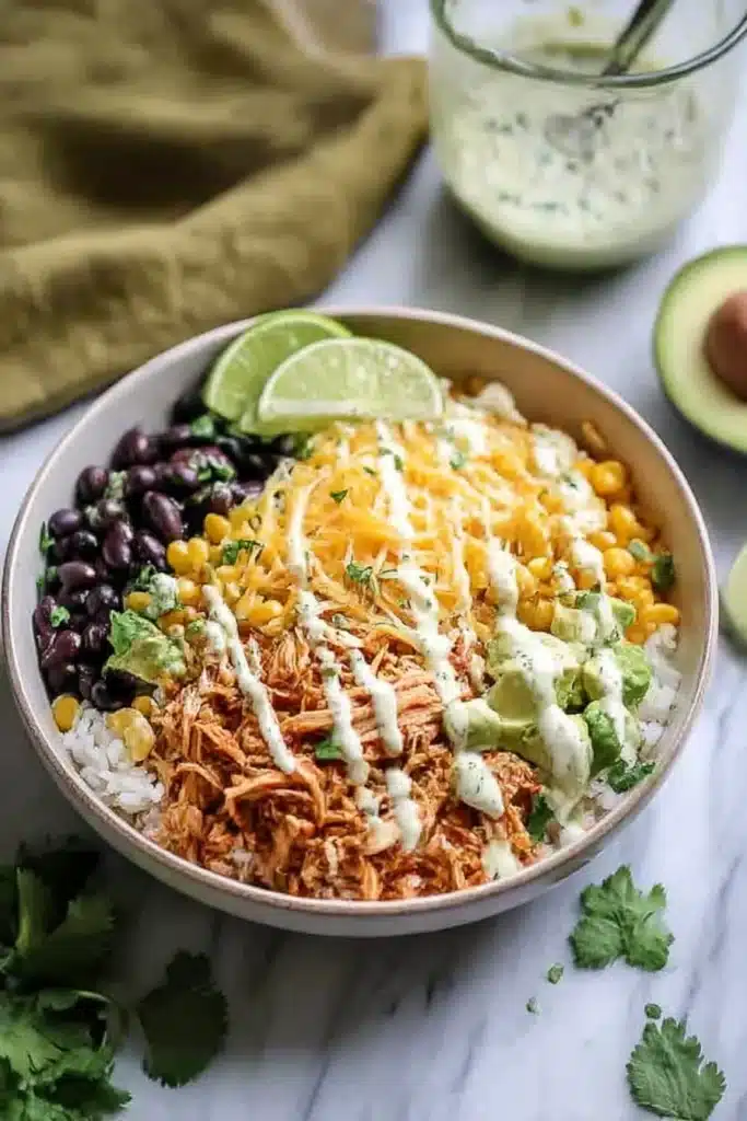 Slow Cooker Chicken Burrito Bowl with black beans, corn, avocado, lime, and creamy dressing on marble surface