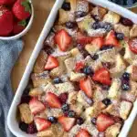 Berry French Toast Casserole | Easy & Delicious Brunch 11 Overhead view of Berry French Toast Casserole with strawberries and blueberries in a white dish, dusted with powdered sugar
