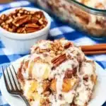 Cinnamon roll dump cake in glass dish with icing, pecans, and silver fork