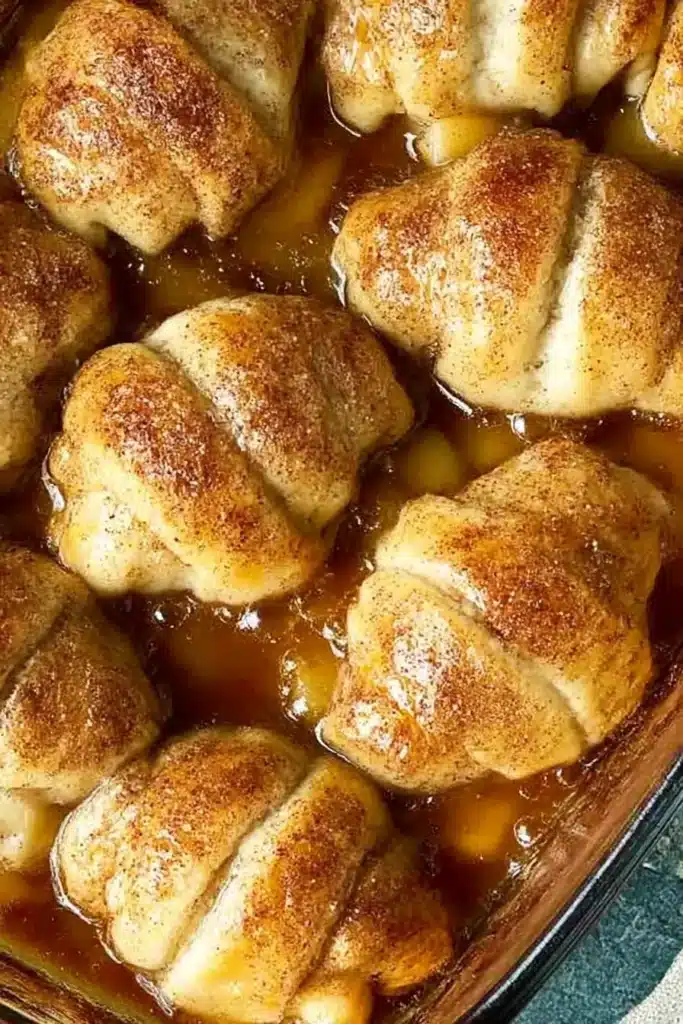 Easy Apple Dumplings – Quick, Cozy & Delicious 6 Baked easy apple dumplings recipe in syrup with golden crescent rolls and cinnamon sugar topping.