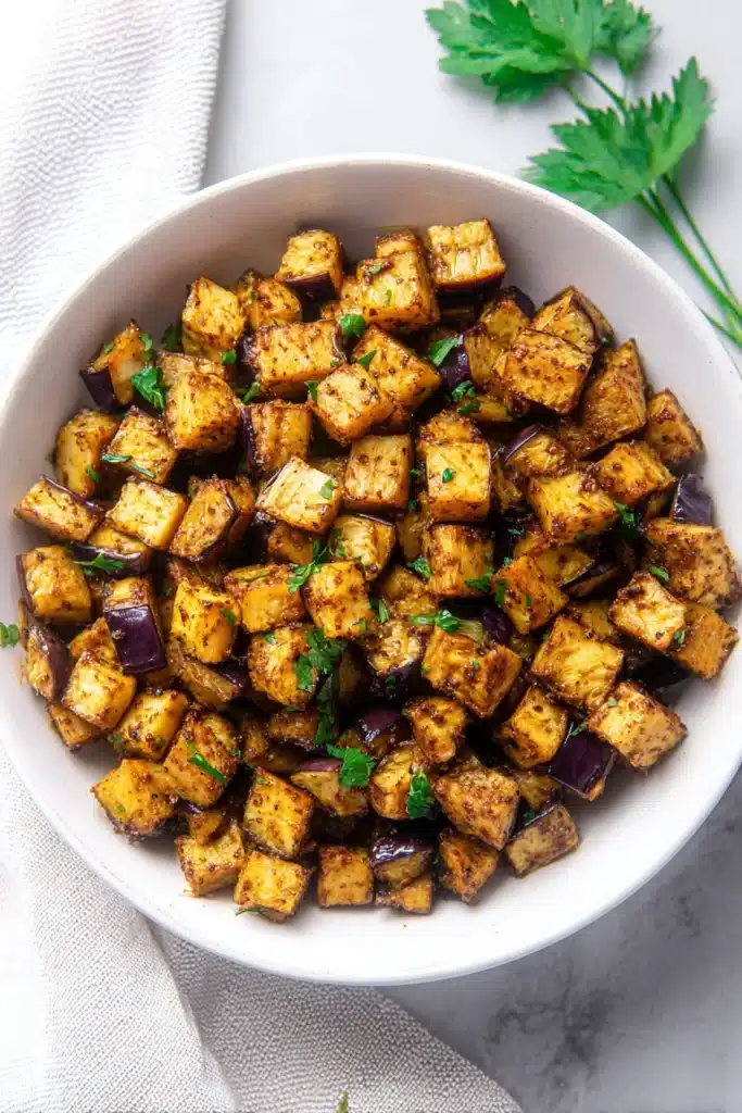 Crispy low-calorie air fryer eggplant cubes in bowl with herbs