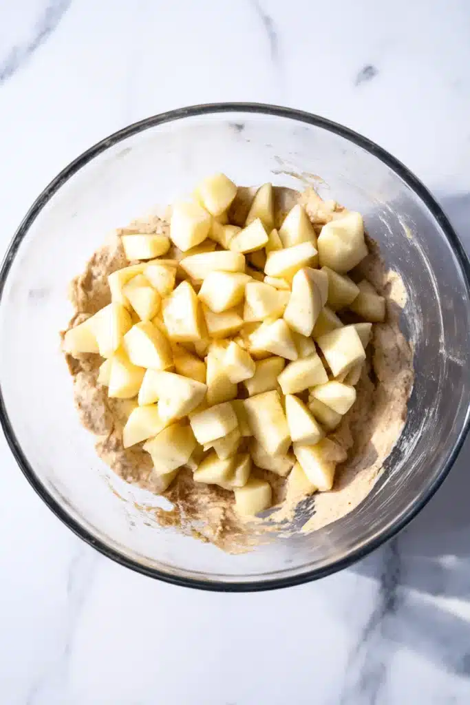 Diced apples on muffin batter in glass mixing bowl