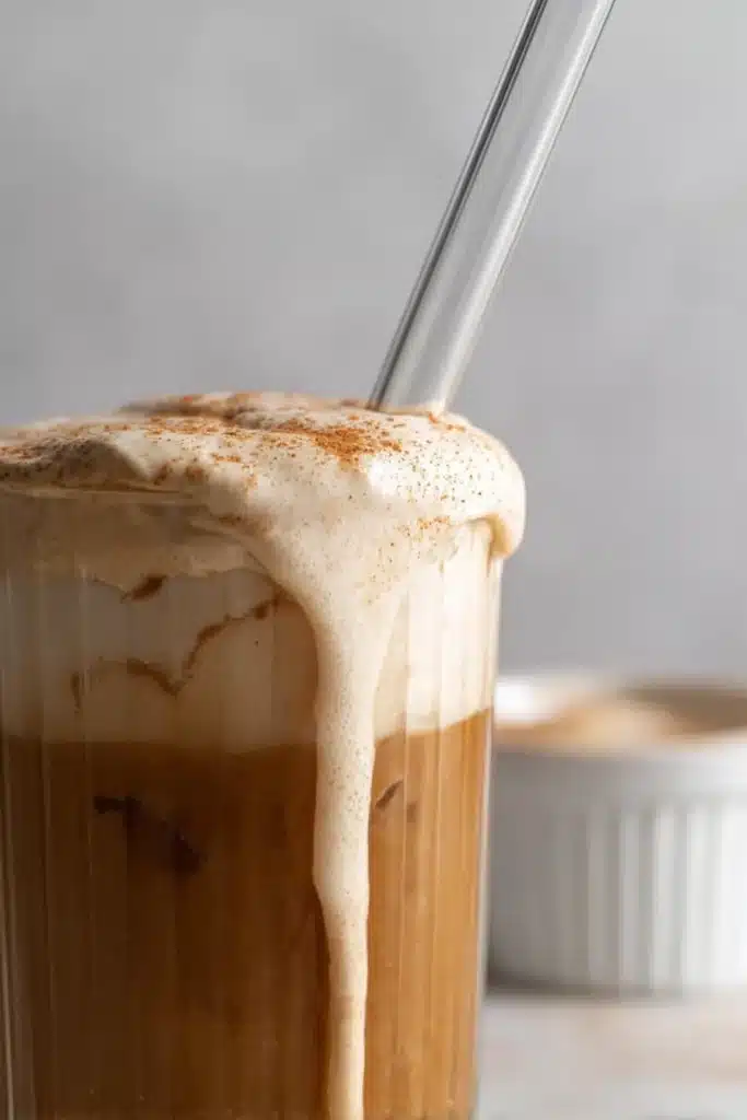 Close-up of pumpkin cream cold brew with dripping pumpkin foam and glass straw