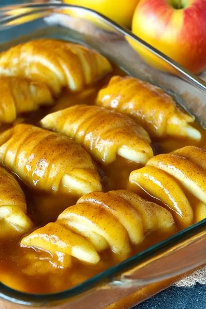 Easy apple dumplings recipe with crescent roll dough and cinnamon sugar syrup, shown unbaked in a glass dish.