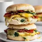 Meal Prep Breakfast Sandwiches That Actually Taste Amazing 5 Meal Prep Breakfast Sandwiches stacked with spinach eggs, crispy bacon, and melted cheese on a ceramic plate