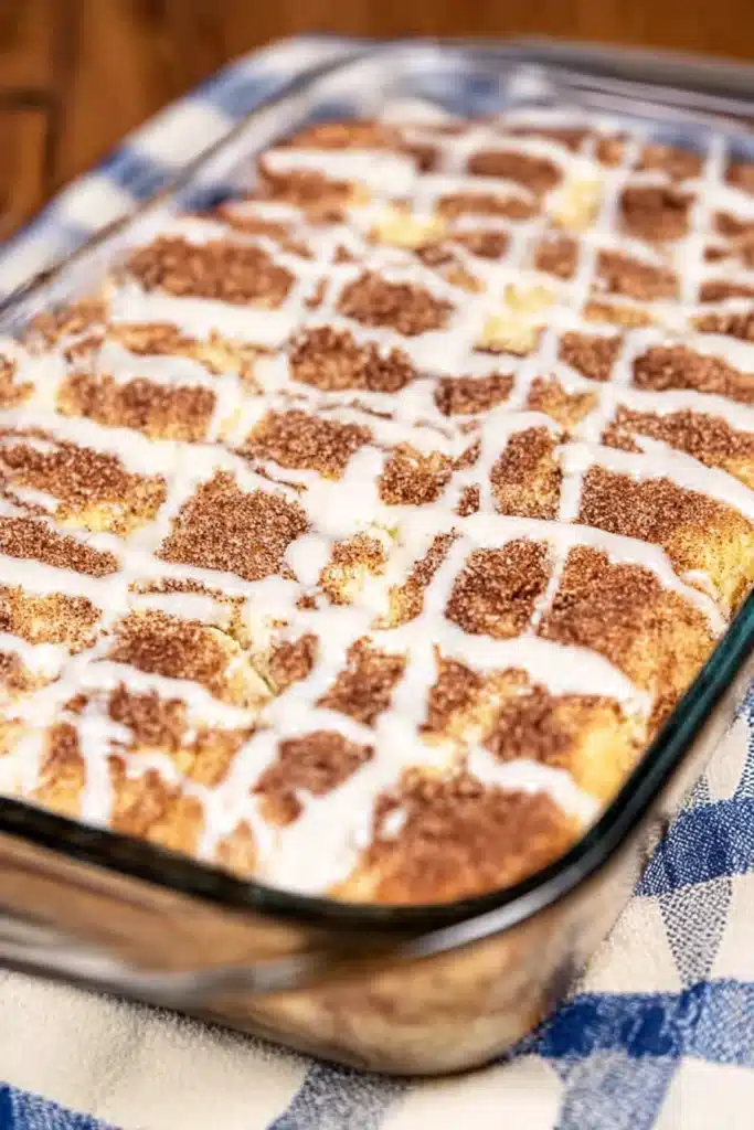 Baked cinnamon roll dump cake in glass dish with icing drizzle