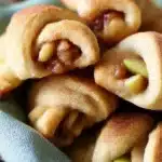 Close-up of golden apple pie bites with flaky crust, apple wedges, and pecans in a rustic blue cloth.