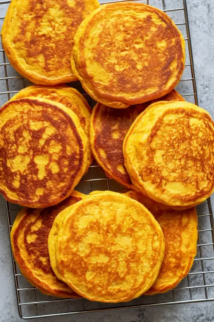 Stack of golden pumpkin cottage cheese pancakes cooling on a wire rack over gray countertop