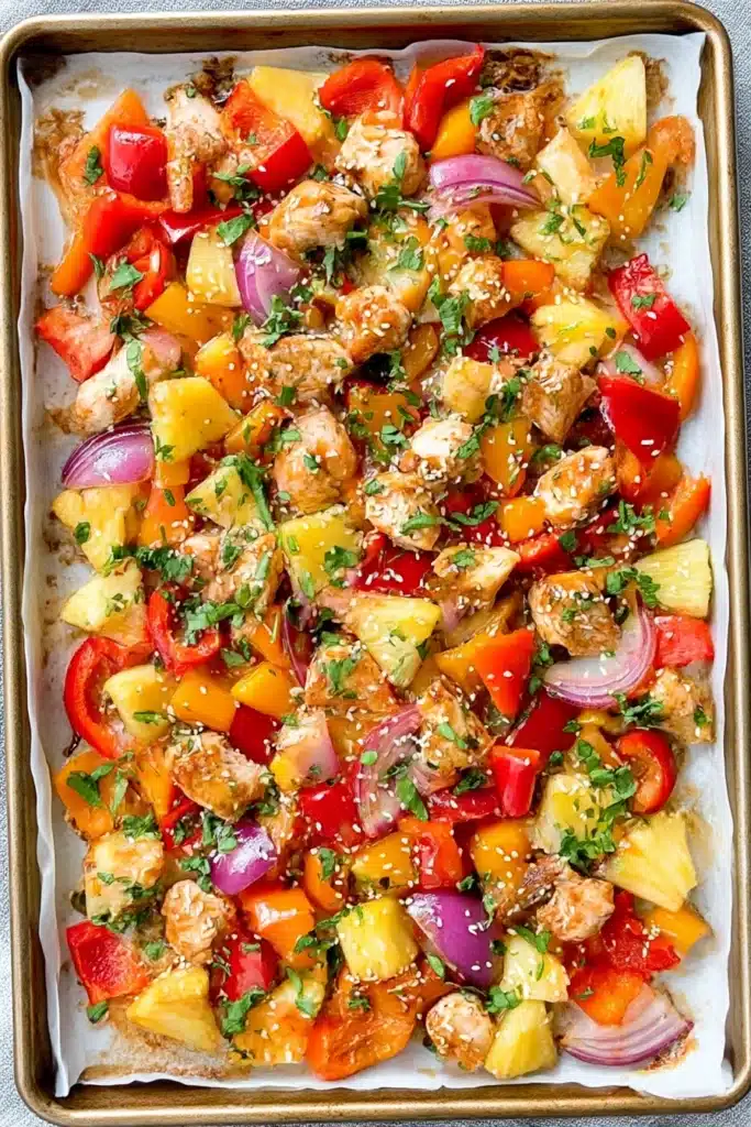 Colorful sheet pan meal with roasted chicken, bell peppers, pineapple, red onion, and sesame seeds