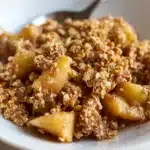 Healthy breakfast apple crumble served on a white plate with small apple chunks