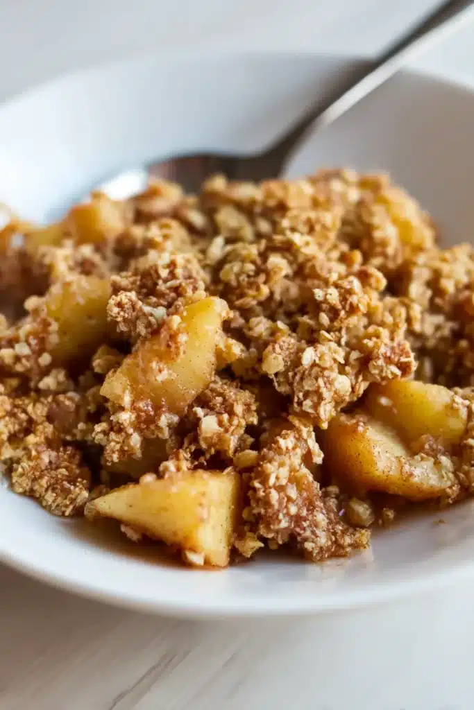 Healthy breakfast apple crumble served on a white plate with small apple chunks