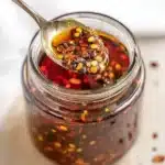 Spoon lifting crispy garlic chili oil from a glass jar