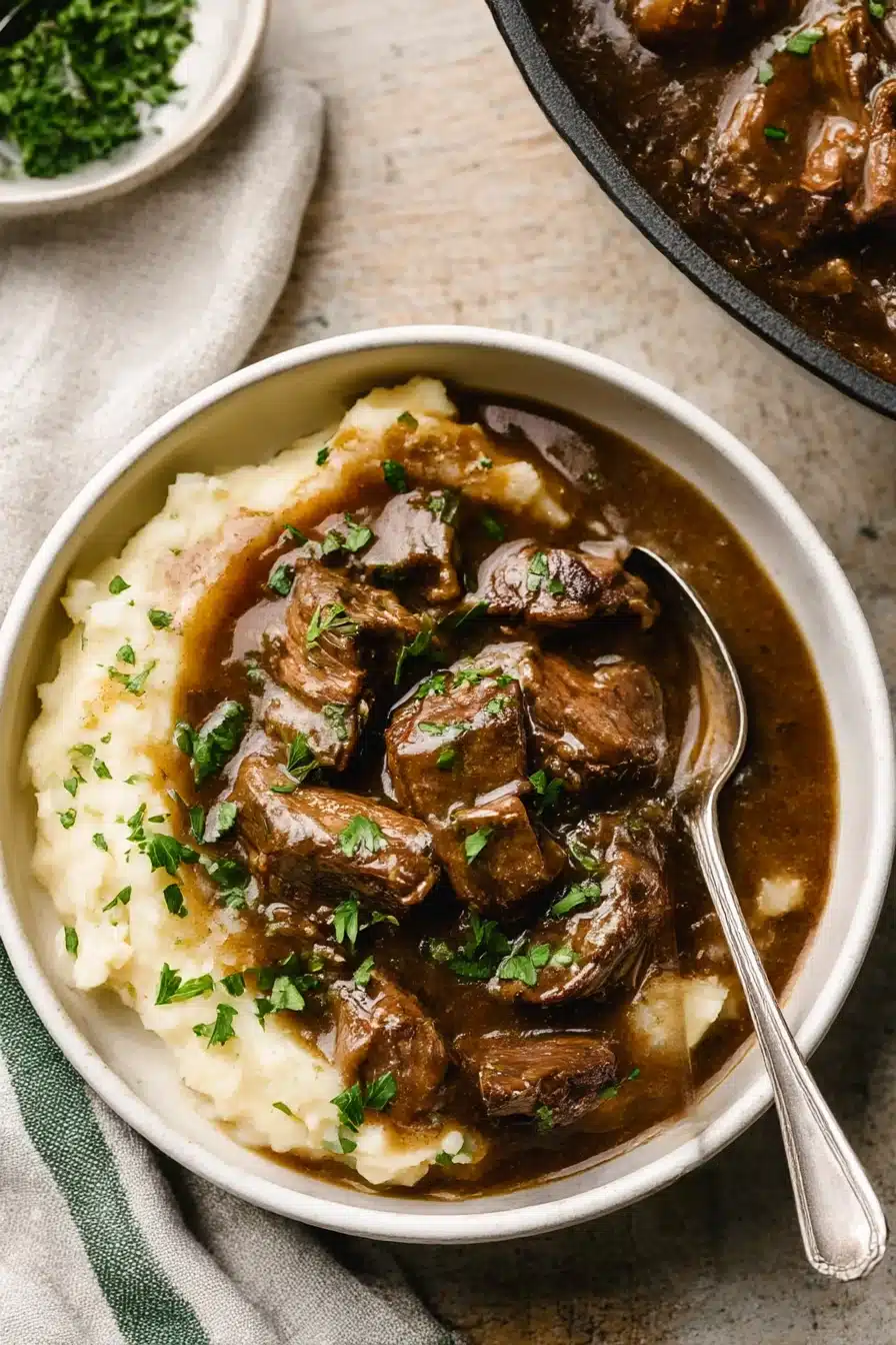 Bowl of Instant Pot beef tips with gravy over mashed potatoes, garnished with parsley