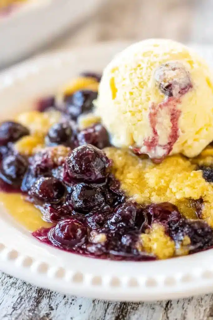 Lemon blueberry dump cake with vanilla ice cream served on a white ceramic plate.