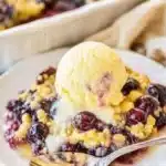 Warm lemon blueberry dump cake with vanilla ice cream on a white dessert plate.