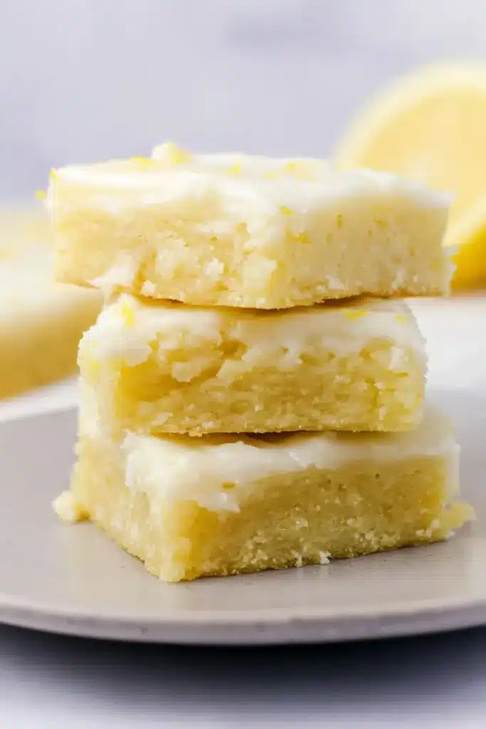 Moist lemon brownies stacked on a plate with glaze topping